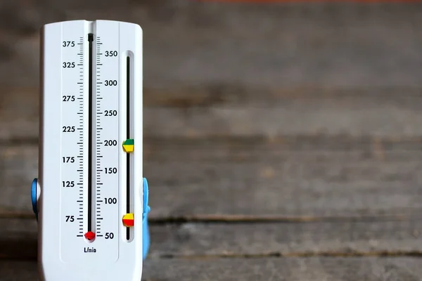 Peak flow meter isolated on wooden background. Hand medical device used to monitor the breath of a person suffering from bronchial asthma. Peak flow meter wide range of values. Breath test allergy. Lung function testing — Stock Photo, Image