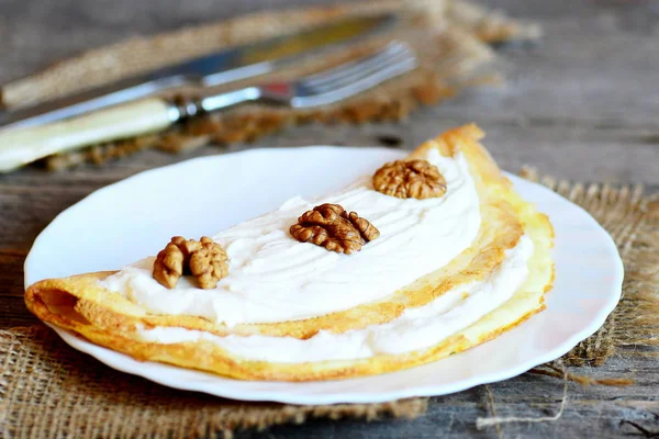 Gefülltes Omelett auf einem Teller, Gabel, Messer, Tuch auf einem Holztisch. Omelette gefüllt mit Quark und Walnüssen. gesundes und leckeres Essen. Gesunder Lebensstil — Stockfoto