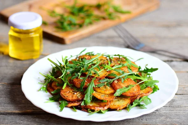 Diiris kentang goreng dengan arugula dan rempah-rempah di piring putih, sebotol minyak zaitun, garpu di atas meja kayu. Resep makanan buatan sendiri. Cottage kentang goreng. Penutup — Stok Foto