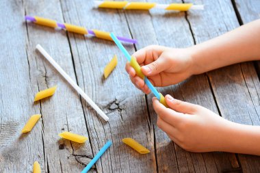 Çocuklar için ince motor becerileri geliştirme. Küçük çocuk bir saman ve pişmemiş makarna elinde tutar. Yaratıcı kids hareket. El ve göz koordinasyonunu geliştirmek için kolay bir egzersiz. Ahşap arka plan 