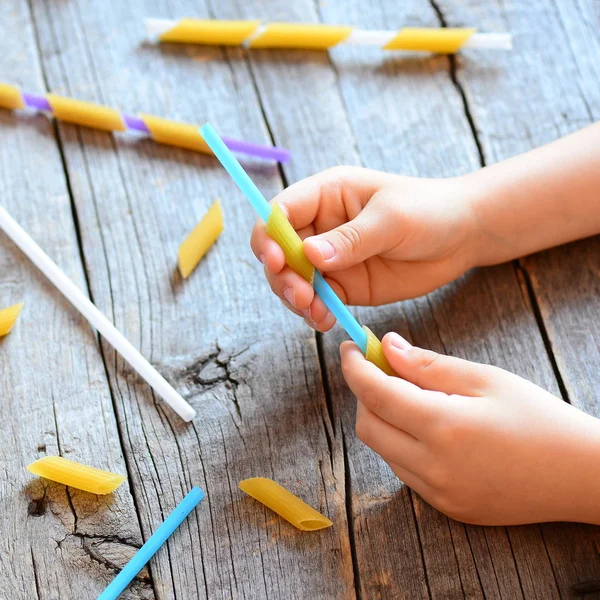 Sviluppo delle capacità motorie nei bambini. Un bambino teneva in mano una cannuccia e una pasta cruda. Attività per bambini. Semplice esercizio. Sfondo in legno — Foto Stock