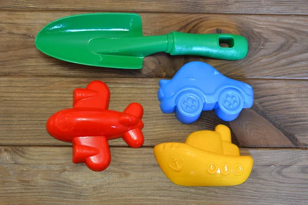Zabawki dla dzieci plaży na brązowym tle drewnianych. Zielony łopata, Czerwony samolot z tworzyw sztucznych, żółty statek z tworzyw sztucznych, niebieski plastykowy samochód — Zdjęcie stockowe