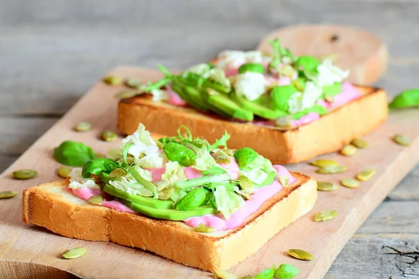 Открытые бутерброды с авокадо на деревянном фоне. Домашние сэндвичи из нарезанного авокадо, свежего салата, базилика и семян тыквы. Вкусный здоровый завтрак рецепт — стоковое фото