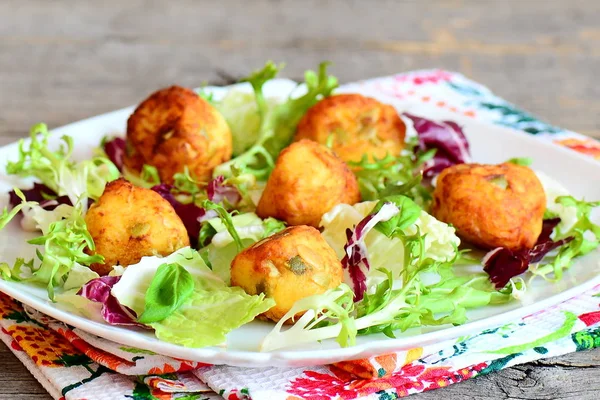 Bolas de patata fritas con mezcla de hojas de ensalada y albahaca en un plato. Pequeñas bolas doradas fritas hechas de puré de papas, huevos, harina, sal y semillas de calabaza. Plato vegetariano. Primer plano. — Foto de Stock