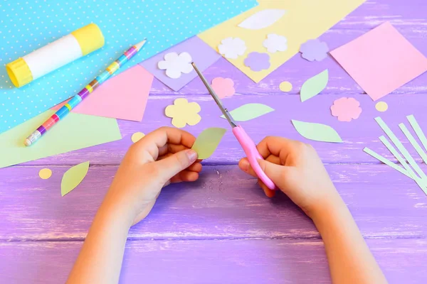 Małe dziecko robi kartkę z życzeniami dla mamy. Krok. Dzieciak trzyma nożyczki w ręku i tnie liść z papieru. Kolorowy papier, szablony papieru, klej, ołówek na stole. Dzień Matki lub 8 marca rzemieślnicze diy — Zdjęcie stockowe