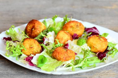 Kızarmış patates topları taze marul ve fesleğen bir plaka üzerinde ve ahşap arka plan üzerinde kabak çekirdeği ile püre. Hızlı ve lezzetli patates topları tarifi. Portre