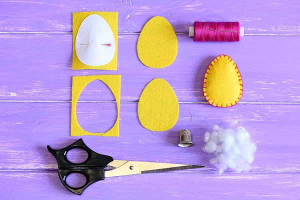 Como fazer uma decoração de ovo de Easter de um sentido. Guia de costura DIY. O amarelo sentiu o ofício de ovo de Easter, cortou partes sentidas na forma de um ovo, molde de papel, tesoura, linha, agulha, dedal, enchedor em uma mesa de madeira. Depósito plano — Fotografia de Stock