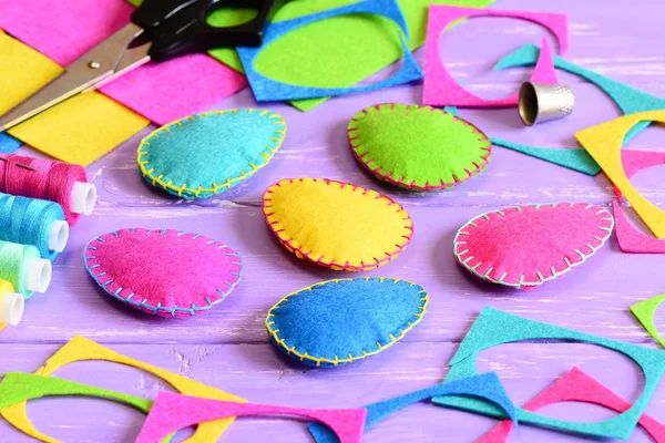 Colorful felt Easter eggs ornaments diy, felt sheets and scraps, scissors, thread, thimble on a table. Easy Easter crafts idea for kids. Abstract Easter eggs craft background. Sewing craft tools workplace Stock Image