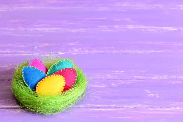 Пасхальные яйца в гнезде. Цветные войлочные пасхальные яйца умирают в зеленом гнезде сизаля, изолированном на фиолетовом деревянном фоне с копировальным пространством для текста. Дети ручной работы яркие пасхальные яйца минимальный фон — стоковое фото