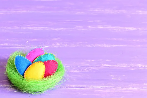 Ostereier in einem grünen Nest. Geschmückte Ostereier aus Filz in einem grünen Sisalnest isoliert auf violettem Holzhintergrund mit Textkopien. Heller festlicher Hintergrund. Kinder basteln zu Ostern — Stockfoto
