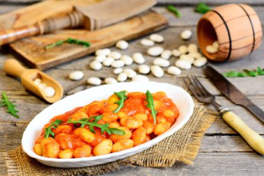 Bir tabak ve vintage ahşap masa fasulye güveç. Beyaz fasulye havuç ve domates sosu ile Komposto ve taze roka ile servis edilir. Lezzetli ve doyurucu vejetaryen fasulye tarifi. Rustik tarzı. Portre