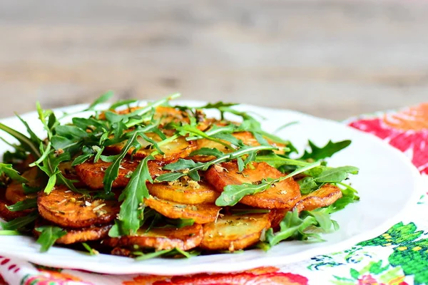 Patatas doradas con rúcula en un plato. Patatas asadas redondas con rúcula fresca y condimentos. Receta de papa rápida y sabrosa. Primer plano. — Foto de Stock