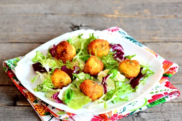 Pequeñas bolas de patata dorada en un plato y mesa de madera rústica. Deliciosas bolas de papa frita con semillas de calabaza servidas con ensalada fresca y hojas de albahaca. Decoración de papa vegetariana — Foto de Stock