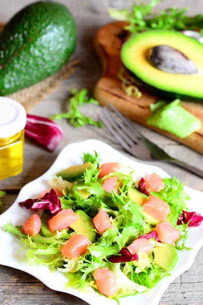 Ensalada de salmón ahumado con mezcla de lechuga, aguacate fresco y aceite de oliva y aderezo de limón en un plato. Ingredientes en una mesa de madera. Ensalada saludable y sabrosa idea. Foto vertical. Primer plano. — Foto de Stock