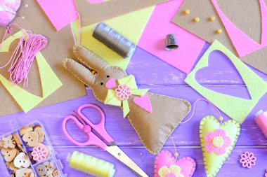 Paskalya tavşanı yürekleri hissettim. Paskalya duvar dekor fikir. Makas, iğne, iplik makaralar, yüksük, düğmeler ve boncuk, renkli bir kutu içinde bir tablo yaprak hissettim. Paskalya dikiş el sanatları arka plan. Üstten Görünüm