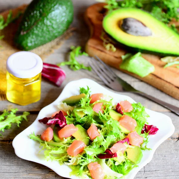 Ensalada de salmón, aguacate y lechuga. Ensalada casera con rodajas de salmón, aguacate fresco y hojas de lechuga se mezclan en un plato. Aguacate, aceite de oliva, tenedor en una mesa de madera — Foto de Stock