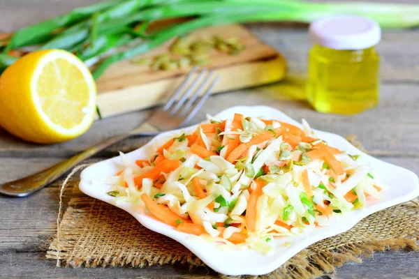 Gesunder Gemüsesalat auf einem Teller. Salat mit frischem Kohl, Karotten, grünen Zwiebeln und Kürbiskernen. Gabel, Zitronenhälfte, Olivenöl im Glas, grüne Zwiebeln auf Holztisch — Stockfoto