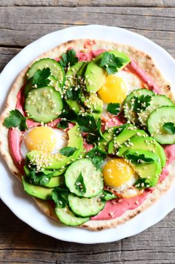 Tortilla yüksek kazıklı kızarmış bıldırcın yumurtası, avokado, salatalık, susam ve maydanoz ve pancar Humus ile yiyeceğim. Kase, çatal vintage ahşap zemin üzerine yarım avokado, pancar humus. Üstten Görünüm