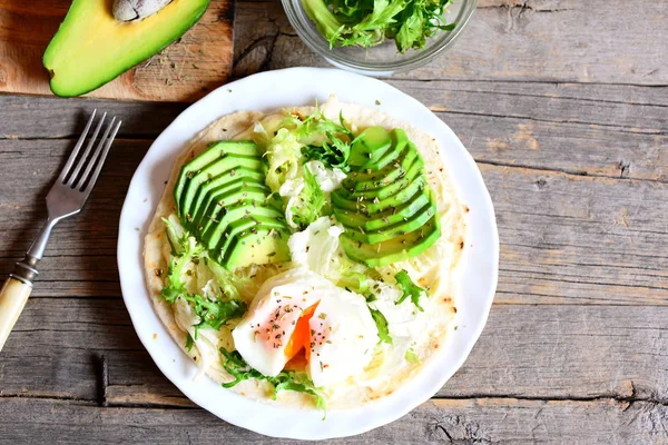 Huevo escalfado, aguacate fresco, ensalada, col china, especias, salsa en una tortilla. Tortilla vegetariana con relleno en un plato aislado sobre fondo de madera vieja con espacio de copia para texto. Vista superior — Foto de Stock