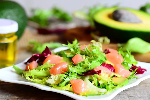 Ensalada de dieta con rodajas de salmón, aguacate fresco y hojas de lechuga se mezclan en un plato. Mitad aguacate fresco, frasco de aceite de oliva en mesa vintage. Primer plano. — Foto de Stock