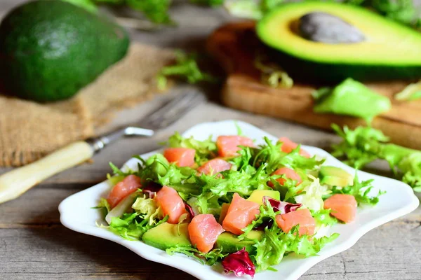 Ensalada de salmón, aguacate y lechuga mixta. Ensalada rápida con rodajas de salmón, aguacate fresco y hojas de lechuga se mezclan en un plato. Aguacate y la mitad, tenedor en una mesa de madera vintage. Primer plano. — Foto de Stock