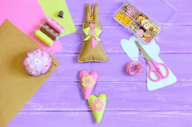 Dolma Paskalya bunny oyuncak üzerinden dikili yürekleri hissettim. Makas, iğne, iplik, yüksük, düğmeler ve kutusunda, kağıt şablonu, boncuk Lila ahşap masa üzerinde yaprak hissettim. Çocukların Paskalya zanaat. Üstten Görünüm