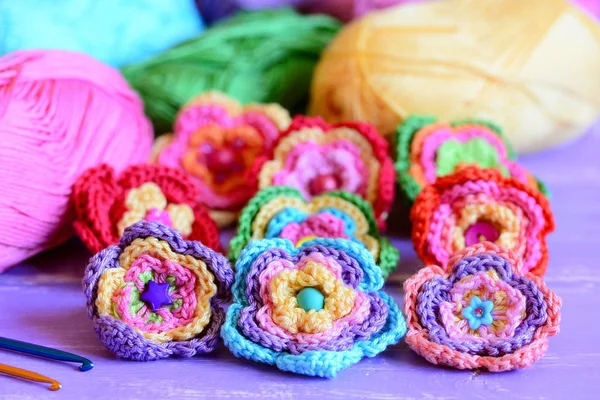 Colorful crochet flowers collection. Crochet flowers, multicolored cotton yarn, crochet hooks on purple wooden table. Easy summer handmade crafts idea. Closeup — Stock Photo, Image