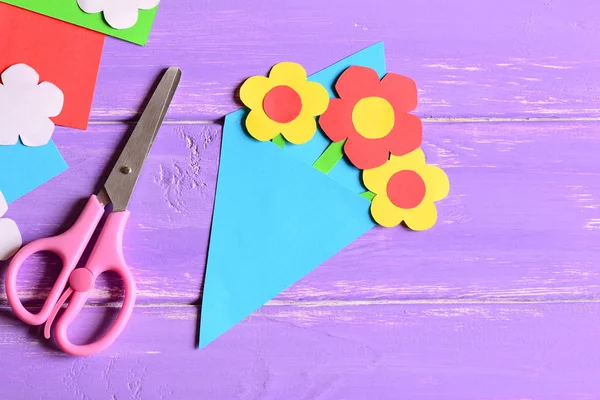 Creating paper crafts for mother\'s day or birthday. Step. Instruction. Paper bouquet gift for mom, scissors on a wooden background with copy space. Simple kids crafts concept. Top view. Closeup