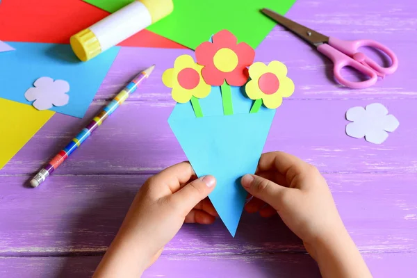 Kleine Kinder bastelten Papierbasteleien für den Muttertag oder Geburtstag. Kind hält Papierstrauß in Händen. einfaches und schönes Geschenk für Mama. Schere, Klebestift, Blumenschablonen, Bleistift auf Holztisch — Stockfoto