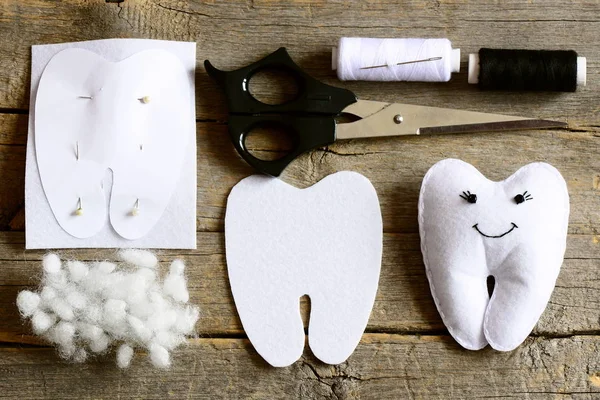 Felt tooth fairy, paper template, felt piece in a tooth shape, scissors, thread, needle, filler on old wooden table. Felt tooth fairy sewing concept. Homemade crafts and toy idea. Top view. Closeup — Stock Photo, Image