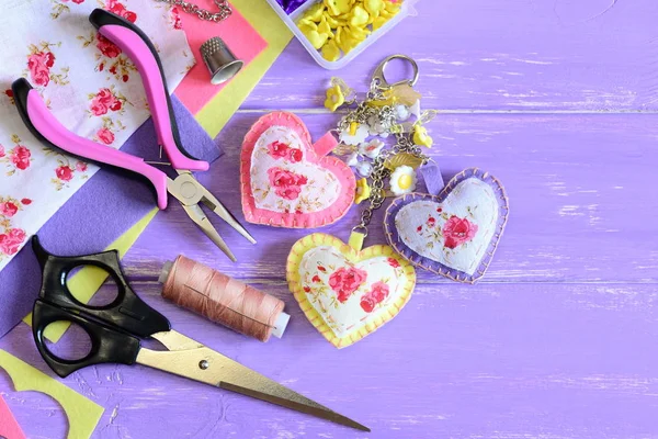 Beautiful hearts keyring. Hand felt and fabric keyring or bag charm. Organizer with plastic flowers, scissors, pliers, felt, needle, thread, scrap. Set for home craft. Wood background with copy space — Stock Photo, Image