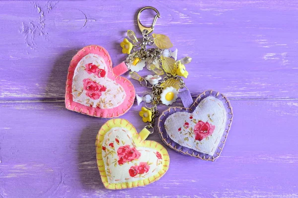 Mooie harten en bloemen keyring. Handgemaakte vilt en stof keyring of tas charme geïsoleerd op Lila houten achtergrond met kopie ruimte voor tekst — Stockfoto