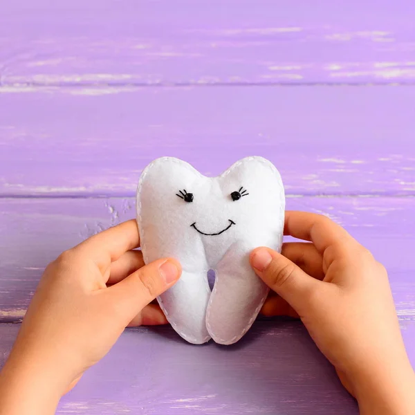 Little child made a felt tooth fairy toy. Child holds a felt tooth fairy toy in his hands. Purple wooden background. Easy and funny kids crafts. Closeup — Stock Photo, Image
