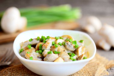 Ekşi krema ve bir kase taze yeşil soğan ile kızartılmış mantar. Vejetaryen yiyecekler. Kolay sağlıklı mantar tarifi. Taze mantar, yeşil soğan, eski ahşap masa üzerinde çatalı. Portre