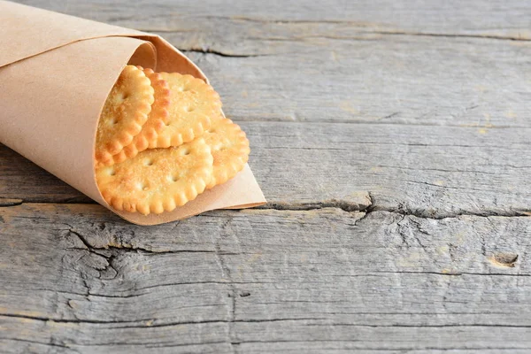 Dry salty crackers in a wrapping paper on a vintage wooden background with copy space for text. Delicious savory crackers snack idea for kids or adults