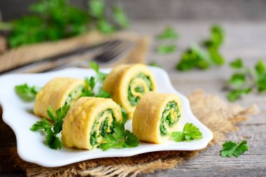 Ev yapımı peynir ve otlar doldurulmuş omlet tabağı ve vintage ahşap bir masa üzerinde. Omlet rendelenmiş peyniri ve ince kıyılmış otlar ile kesti. Lezzetli ve baharatlı kahvaltı omlet tarifi. Rustik tarzı