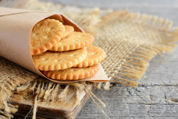 Salty thin crackers in a wrapping paper and on a sackcloth. Vintage wooden background. Tasty crispy crackers snack idea for children and adults