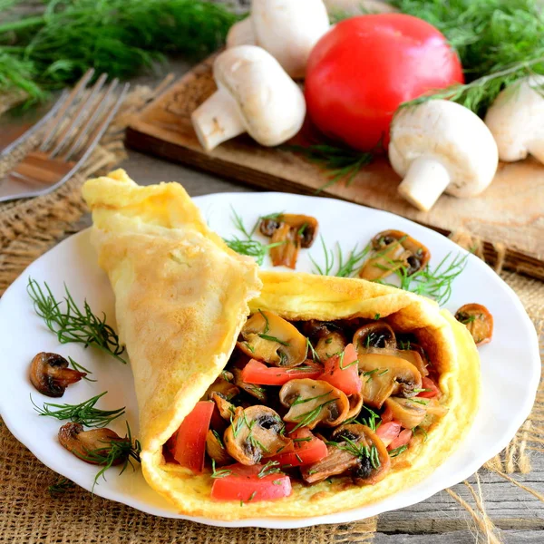 Stuffed omelette on a plate. Homemade omelette with mushrooms slices, tomatoes and dill on a plate, ingredients, fork on a vintage wooden table. Easy and delicious vegetarian breakfast. Rustic style — Stock Photo, Image