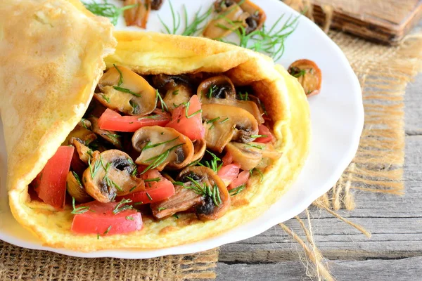 Ricetta omelette funghi facili. Omelette fatte in casa ripiene di funghi, pomodori e aneto su un piatto e fondo in legno antico. Colazione gustosa con uova per tutta la famiglia. Stile rustico. Primo piano — Foto Stock