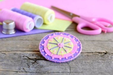 Colorful felt round flower decorated with pink beads. Handmade felt flower, scissors, thread, colorful felt sheets, thimble on vintage wooden background. Simple, fun and quick kids sewing project clipart