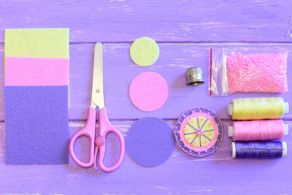 Grazioso fiore rotondo fatto di feltro e perline, cerchi e fogli di feltro colorati, forbici, set di bobine di filo, ago, perline rosa su un tavolo di legno. Guida al cucito. Insegnare cucito per bambini. Vista dall'alto — Foto Stock