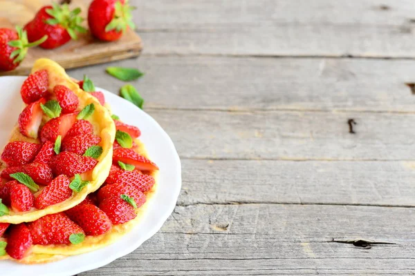 Leicht gefülltes Omelett. gesunde und schnelle Omelette gefüllt mit frischen Erdbeeren und garniert mit Minze auf einem Teller und Holzhintergrund mit Kopierraum für Text. Erdbeer-Omelette-Frühstück — Stockfoto