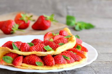 Taze çilek yumurta omlet. Omlet çilek dilimleri ile dolu ve bir plaka üzerinde nane yaprakları ile süslenmiş. Ahşap bir masa üzerinde taze çilek. Temiz yemek tatlı kahvaltı Omlet Tarifi