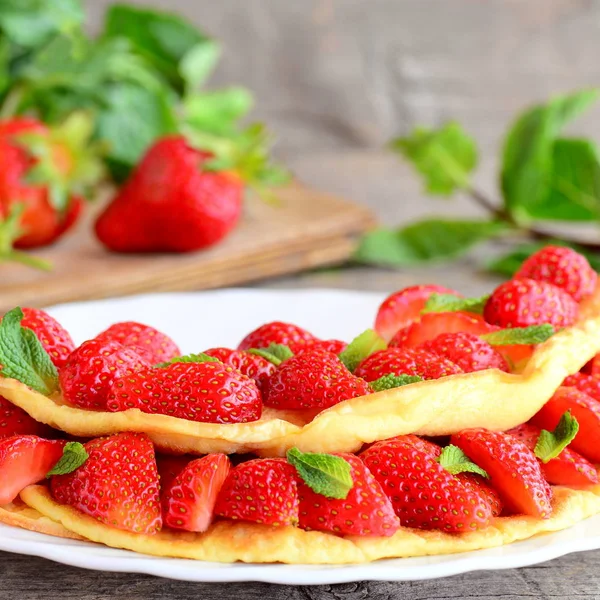 Frisches Erdbeer-Ei-Omelett. Omelett gefüllt mit Erdbeerscheiben und garniert mit Minzblättern auf einem Teller. frische Erdbeeren und Minzblätter auf dem Tisch. süßes Omelett mit Beeren Rezept — Stockfoto