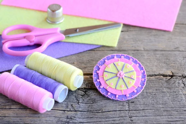 Abstract felt round flower with light pink beads. Handmade bright felt flower, scissors, thread, colorful felt sheets, thimble on old wooden table. Elementary, fun and quick kids hand sewing concept — Stock Photo, Image