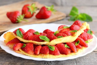 Çilek ile kahvaltı sufle omlet. Kızartılmış omlet ve taze çilek dilimleri ile dolu bir plaka üzerinde nane ile süslenmiş. Eski ahşap masa üzerinde taze çilek. Portre