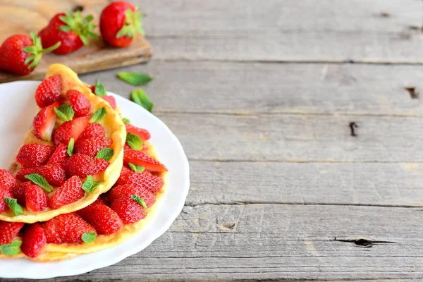 Une omelette aux fraises. Omelette colorée farcie aux fraises fraîches et garnie de menthe sur une assiette et fond en bois avec place vide pour le texte. Petit déjeuner d'été ou idée de déjeuner — Photo