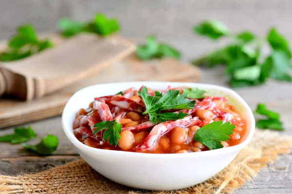 Sausage and bean stew. Easy white bean stewed with smoked sausage, tomato sauce and parsley leaves in a bowl and on a wooden table. Home nutritious stew. Rustic style