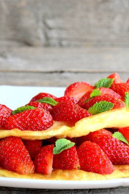 Berry omlet beyaz tabakta. Omlet parlak çilek ile doldurulmuş ve yeşil nane ile süslenmiş. Lezzetli ve kolay yaz kahvaltı. Dikey fotoğraf. Portre
