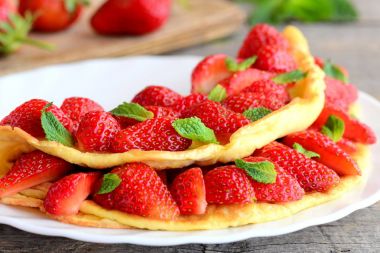 Beyaz bir plaka üzerinde parlak doldurulmuş omlet. Omlet taze çilek ile doldurulmuş ve yeşil nane ile süslenmiş. Lezzetli yaz tarifi. Portre